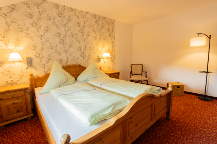 Berggasthof Neues Haus - Doppelzimmer Ein Doppelbett mit zwei Nachtschränkchen und Wandlampen dazu roter Teppich und eine Stehlampe
