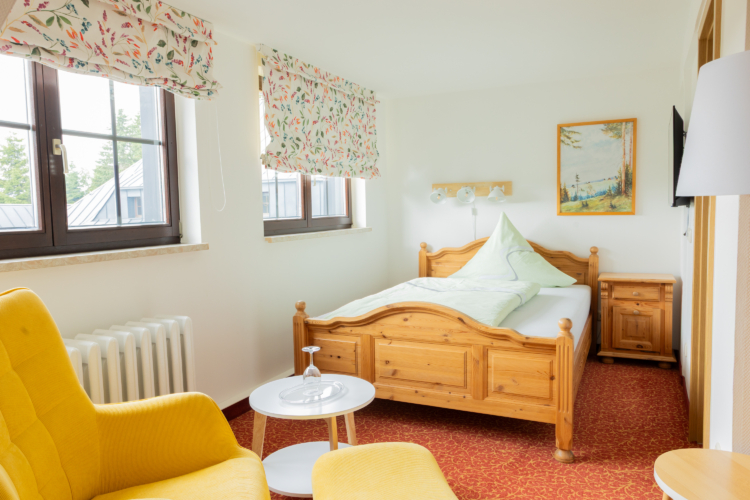 Bergasthof Neues Haus - Einzelzimmer Ein Zimmer in dem ein Bett aus Holz steht. Der Fußboden ist rot und ein gelber Sessel mit kleinem Beistelltisch ist zu sehen.