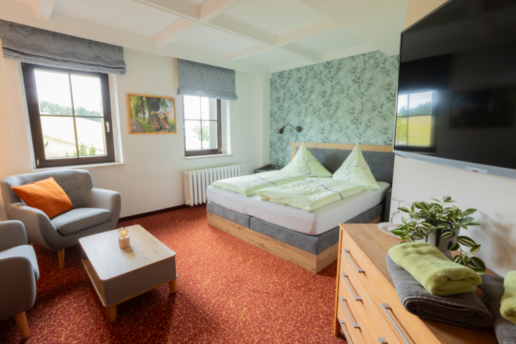 Berggasthof Neues Haus - Familienzimmer Ein Raum mit zwei Sesseln und einem Doppelbett. Es ist weiterhin ein roter Teppich, ein Holztisch, eine Kommode und ein TV zu sehen.